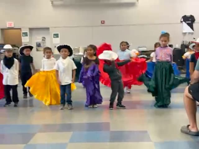 Young students in colorful full skirts and hats performing a Ballet Folklórico dance.