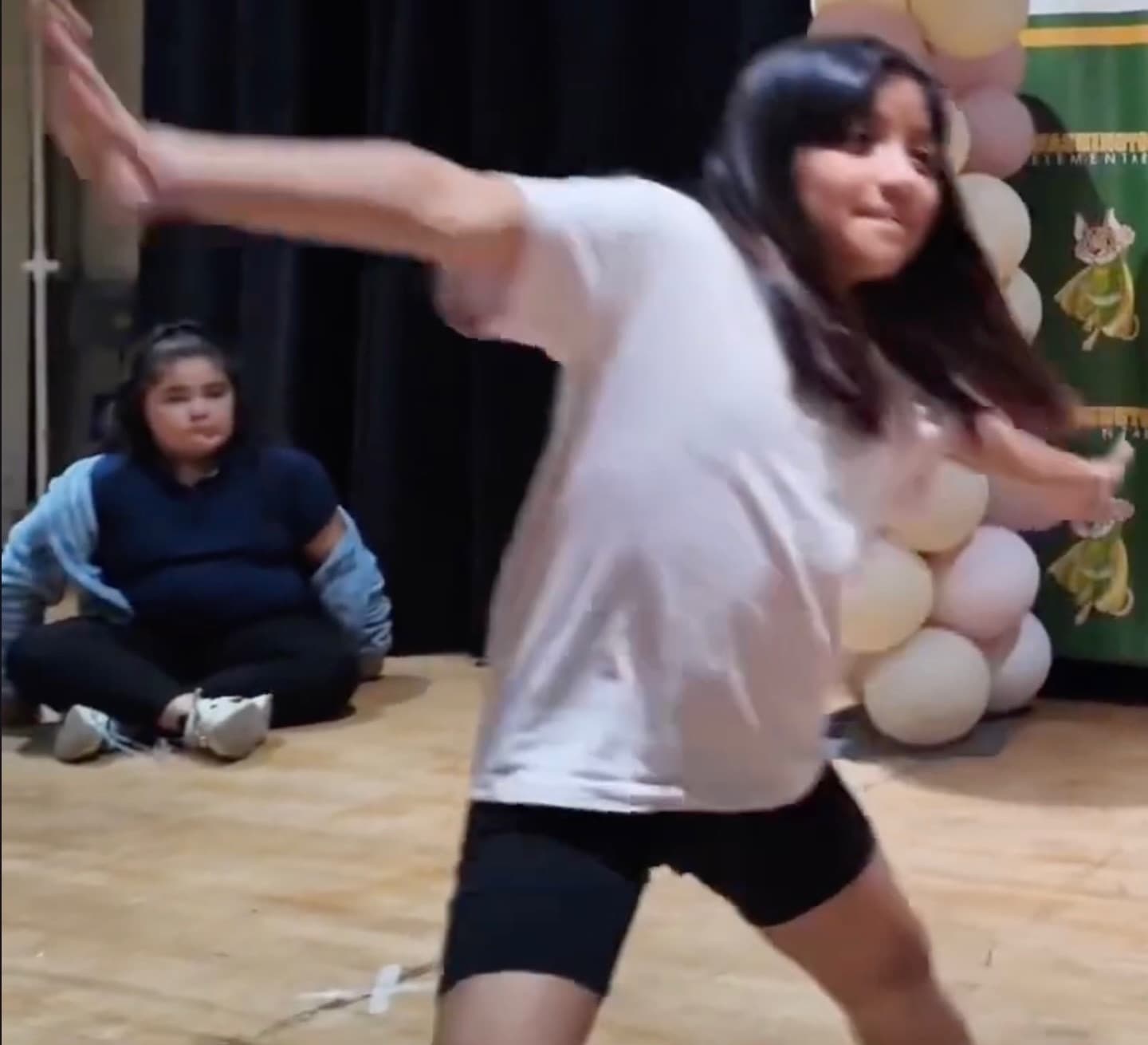 A student dancing with arms extended during an iAttend Dance session while a classmate watches.